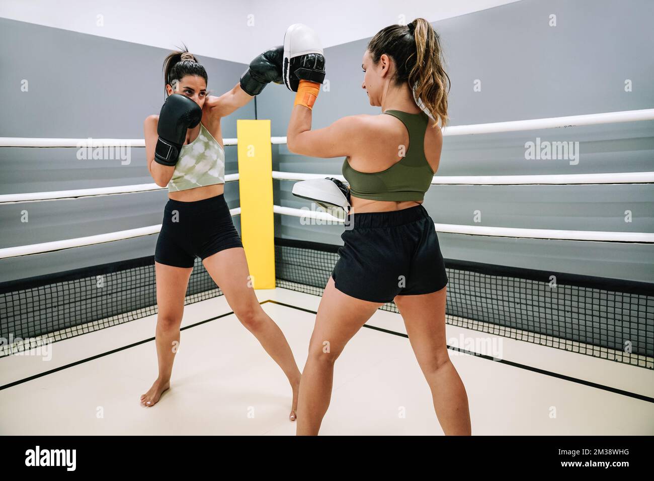 A young student practicing punching with her trainer in a kickboxing practice inside the ring Stock Photo