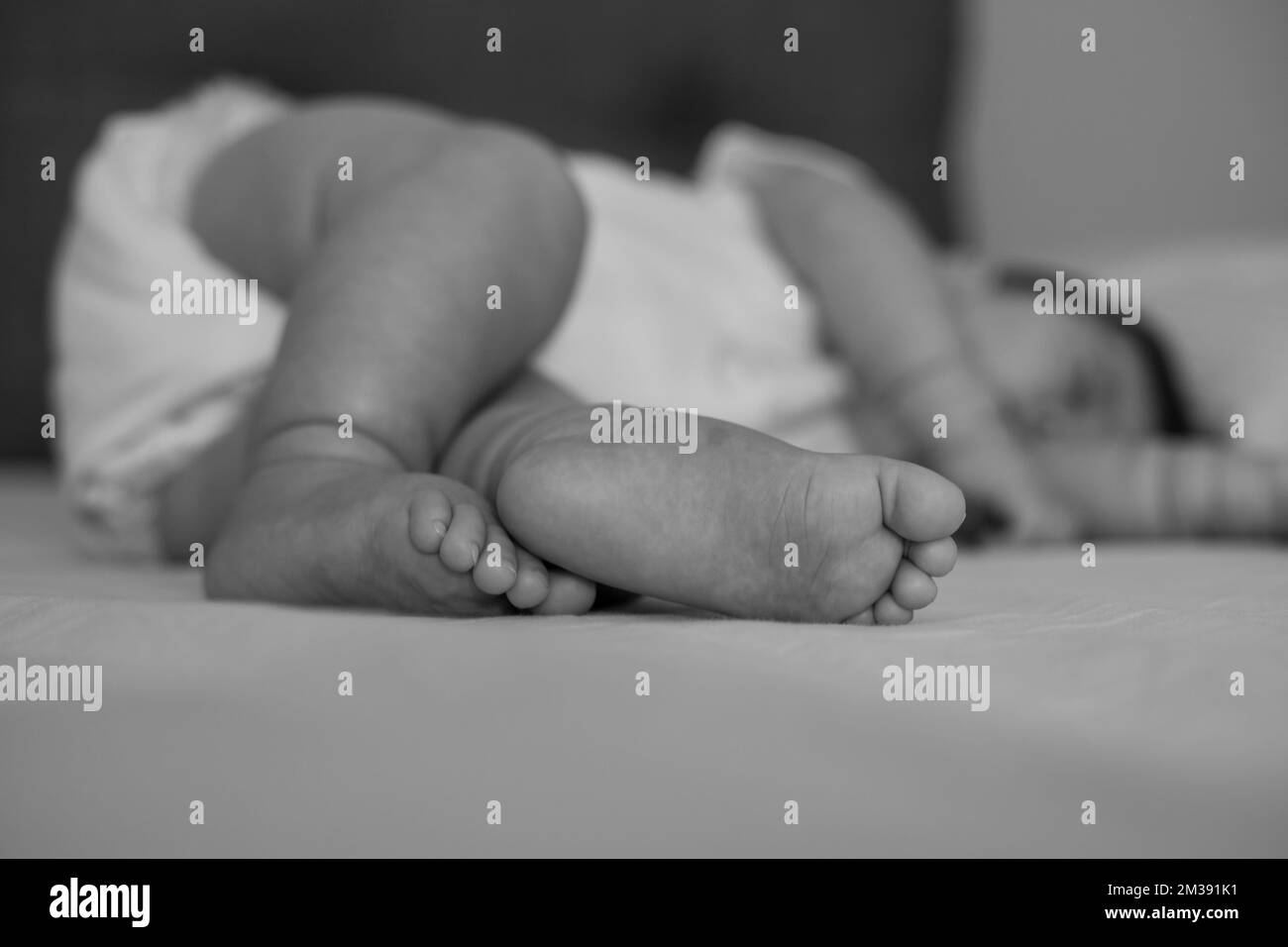 The feet of the baby sleeping on the bed are in focus. Black and white photo. Stock Photo