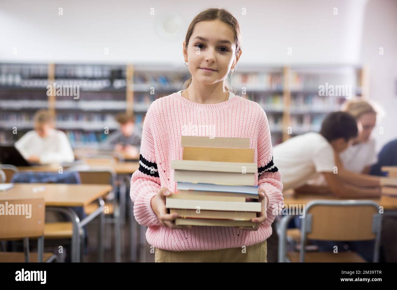 Girl with pile of books in library Stock Photo - Alamy