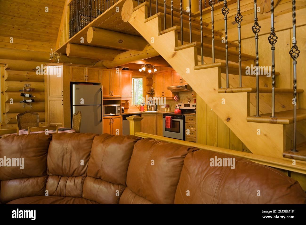 Living room with dark tan leather sofa, kitchen room and pine wood