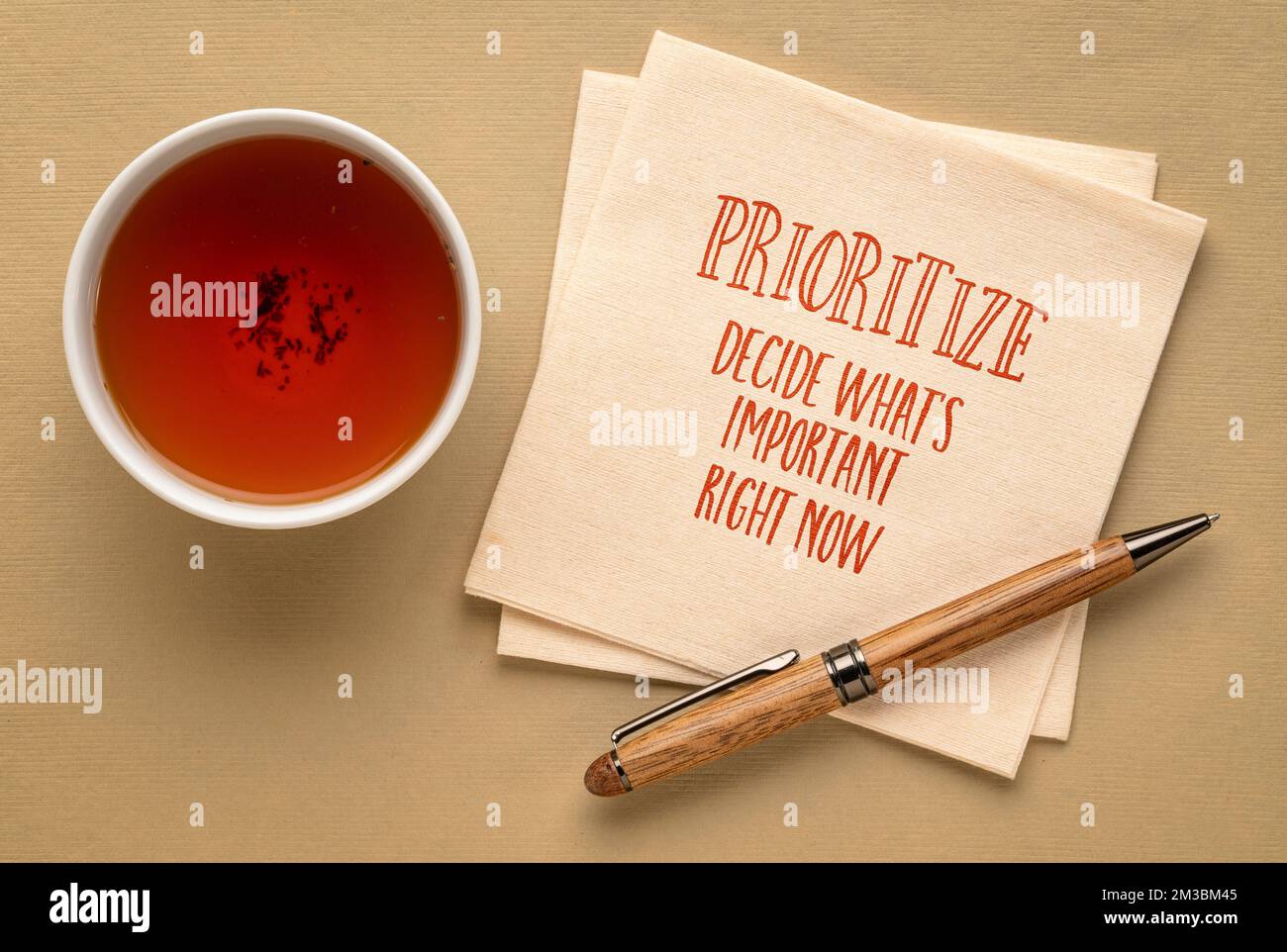 prioritize, decide what is important right now - inspirational advice or reminder on a napkin with a cup of tea, productivity and personal development Stock Photo