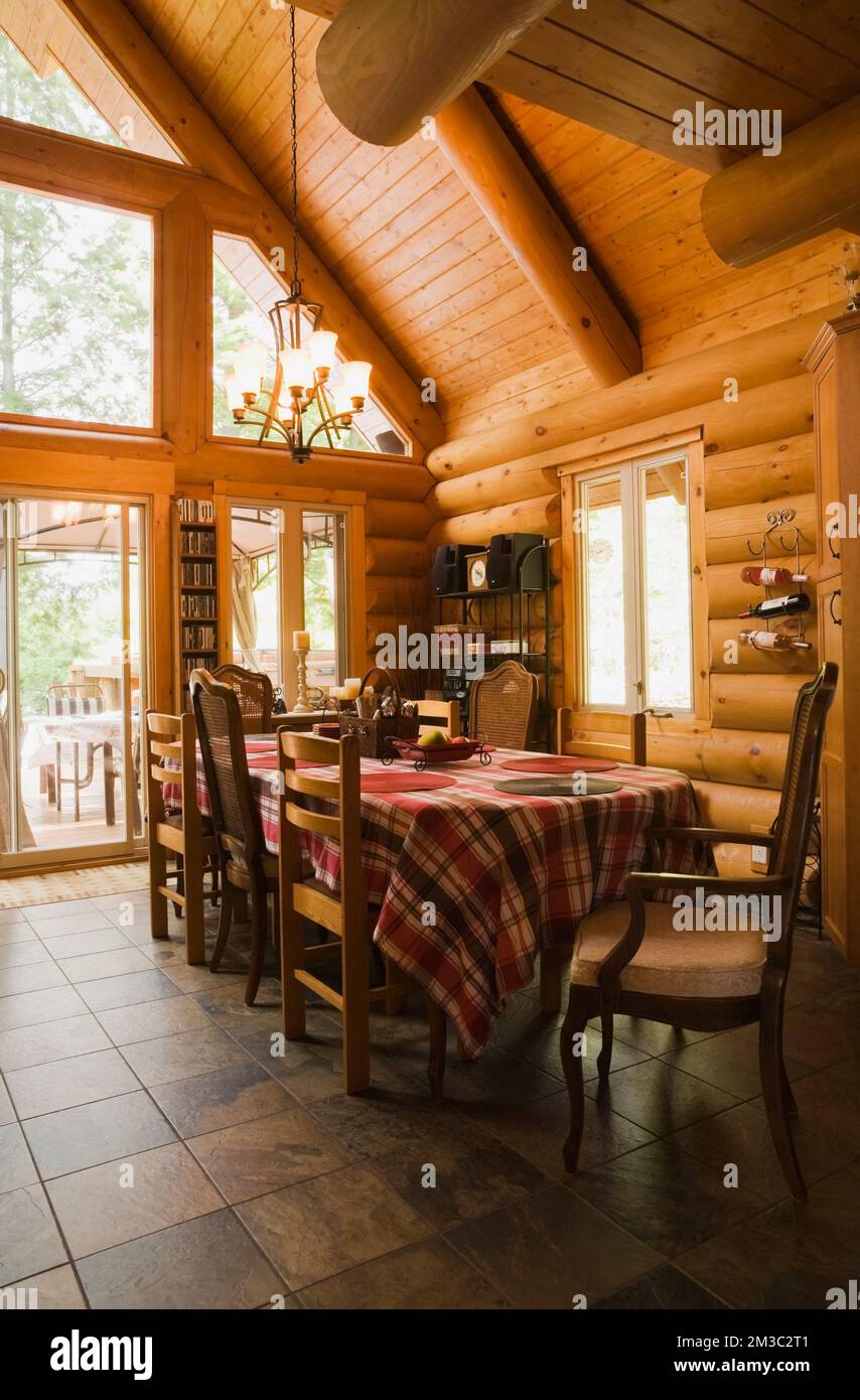 Dining table with red, white and maroon tartan tablecloth and mixed style wood and upholstered chairs in dining room inside contemporary log cabin. Stock Photo