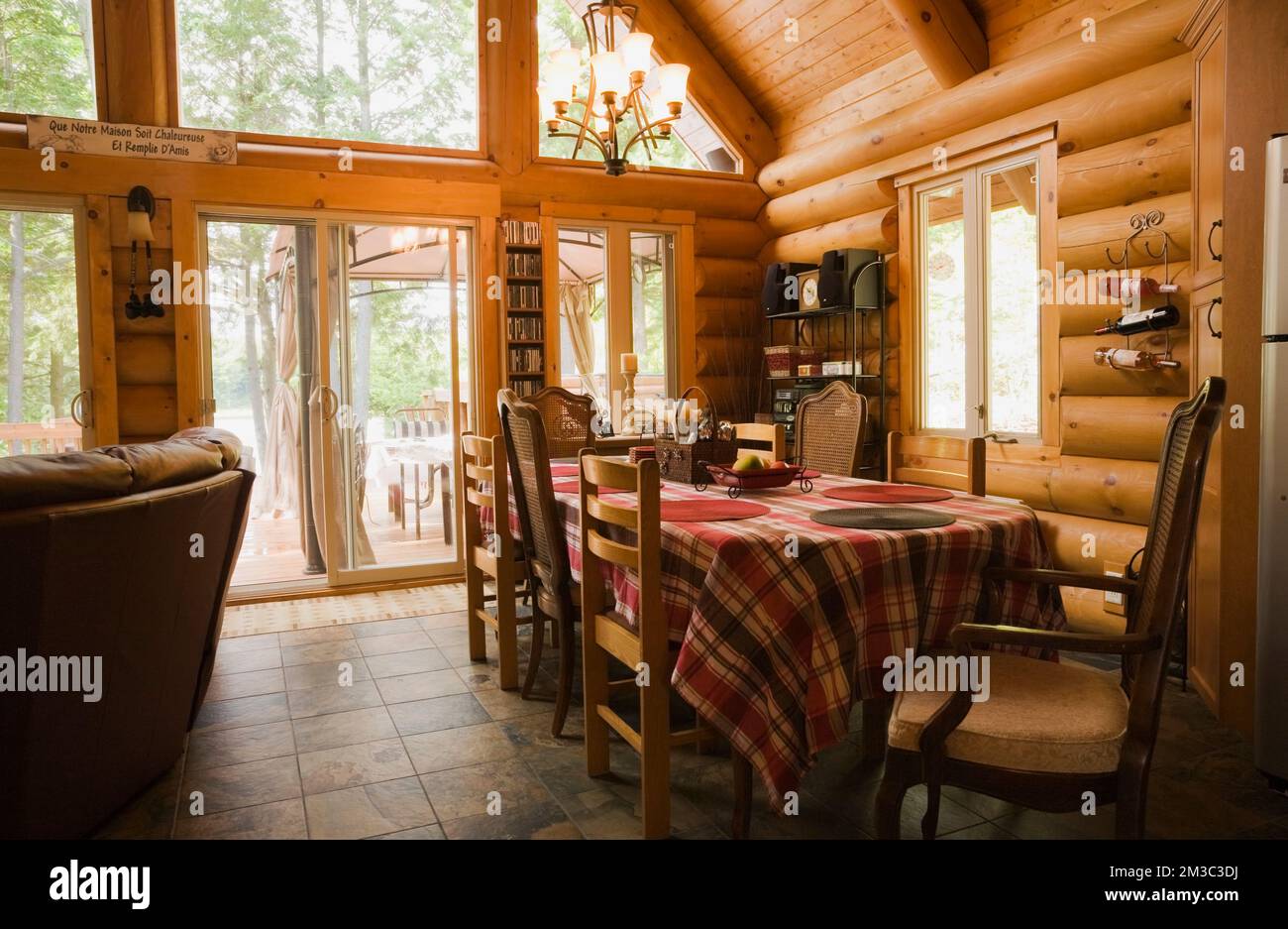 Dining table with red, white and maroon tartan tablecloth and mixed style wood and upholstered chairs in dining room inside contemporary log cabin. Stock Photo