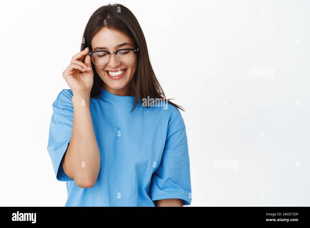 Beautiful young girl student in glasses, trying new eyewear at optic store, standing in blue t-shirt over white background Stock Photo