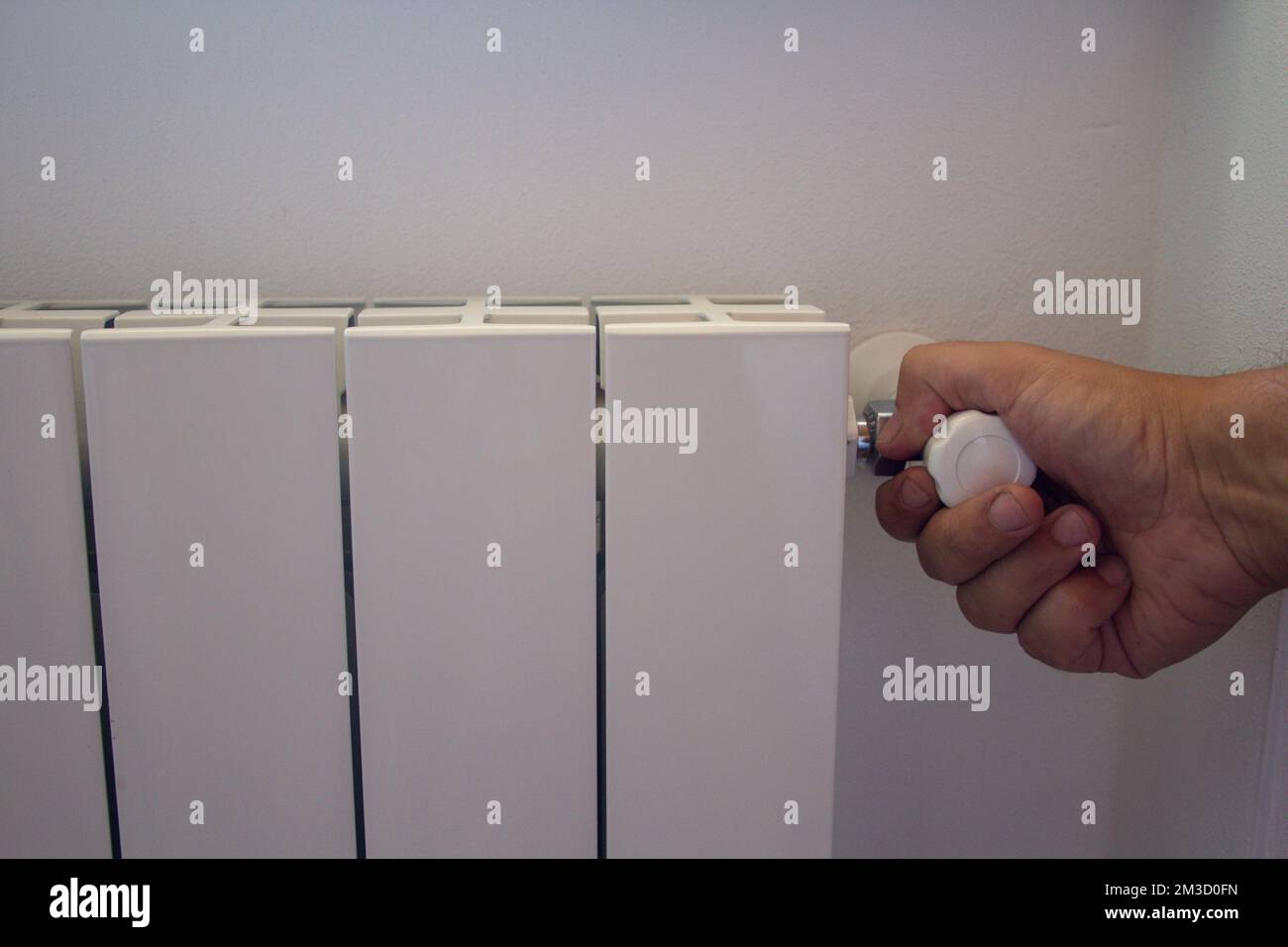 Image of a man's hand closing the knob of a radiator. Problem of the excessive cost of heating