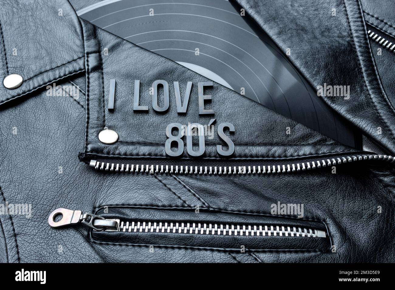 Closeup to a I love 80s lettering art over a black leather biker jacket with LP vinyl disc. Music lover concept, retro photography. Stock Photo