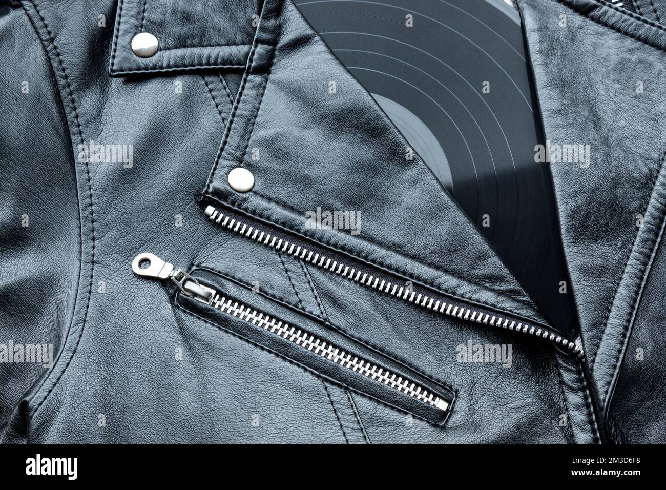Closeup to a black leather biker jacket with LP vinyl disc. Music lover concept, retro photography. Stock Photo