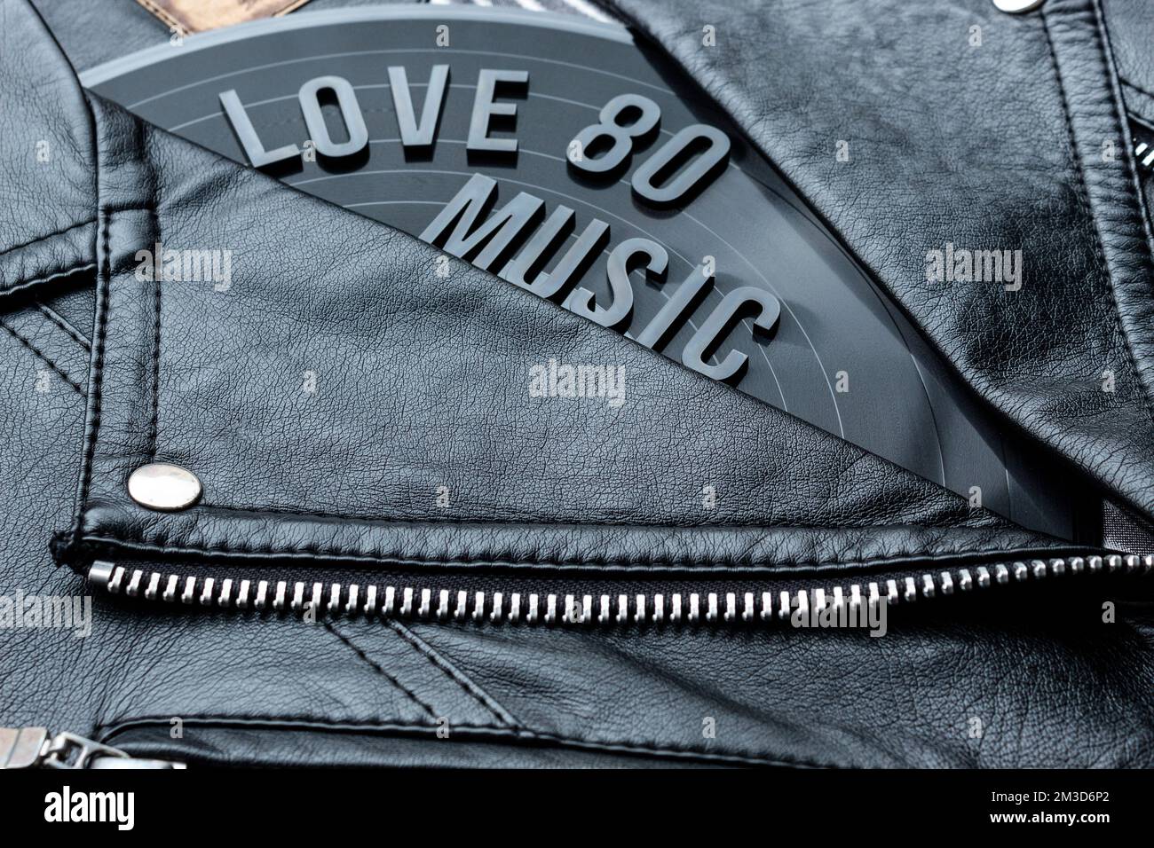 Closeup to a love 80 music lettering art over a black leather biker jacket with LP vinyl disc. Music lover concept, retro photography. Stock Photo
