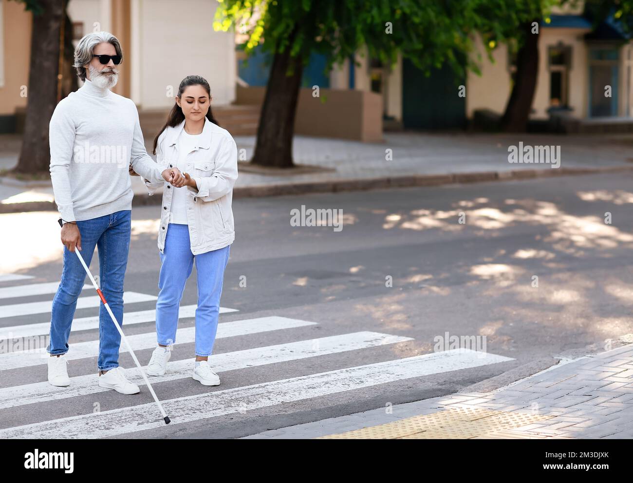 Young woman helping senior blind man to cross road in city Stock Photo