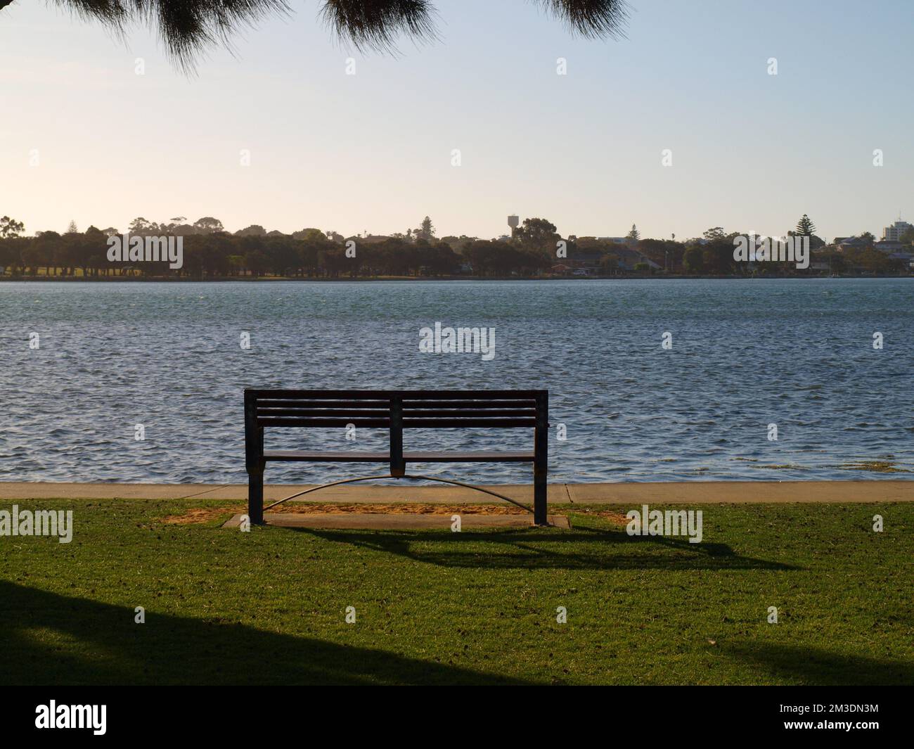 Chair facing the waters of a lake at sunset in Mandurah, Australia. Silhouette, Under exposed. Stock Photo