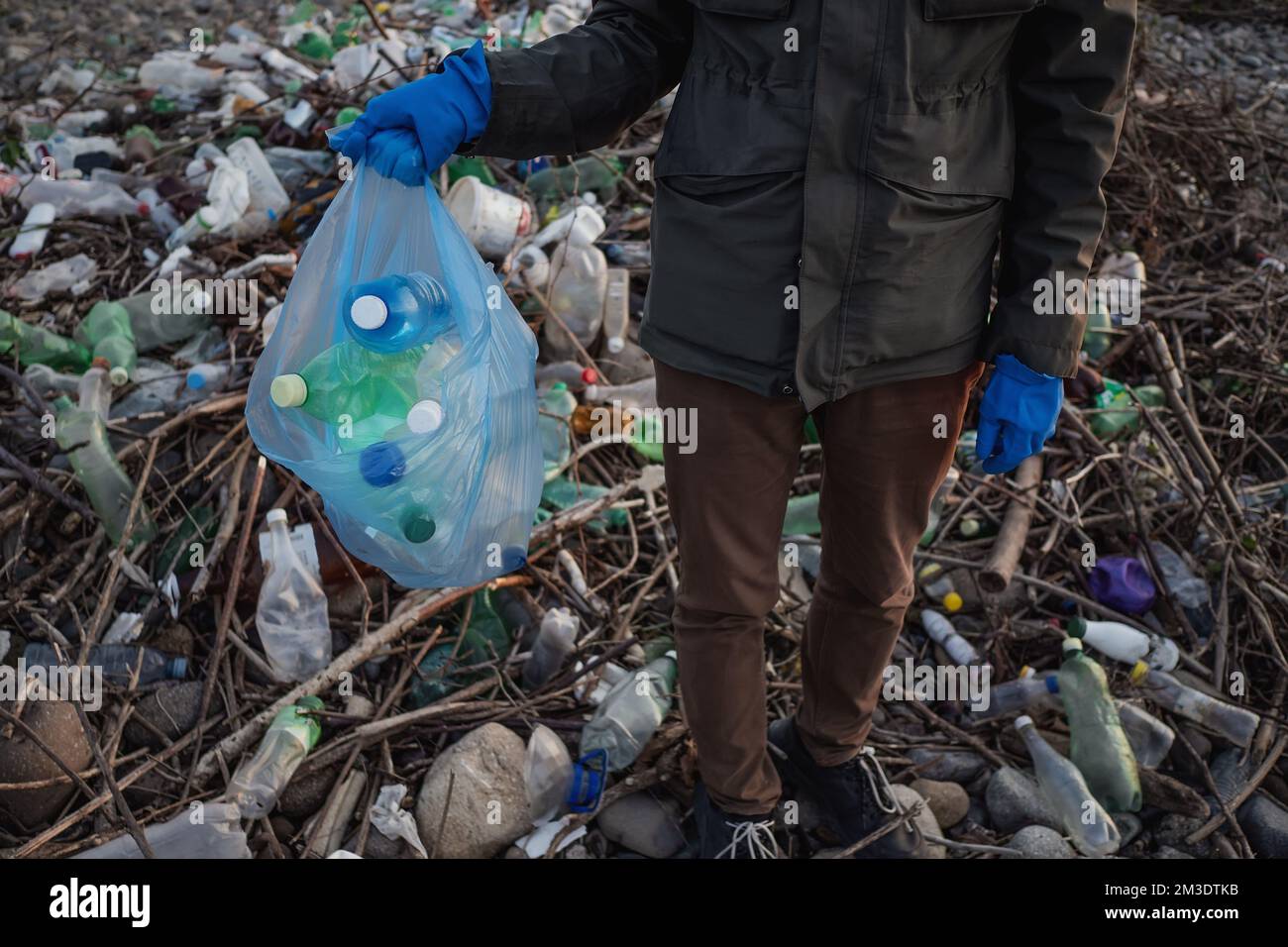 Process of cleaning stone beach from plastic waste. Man holds plastic