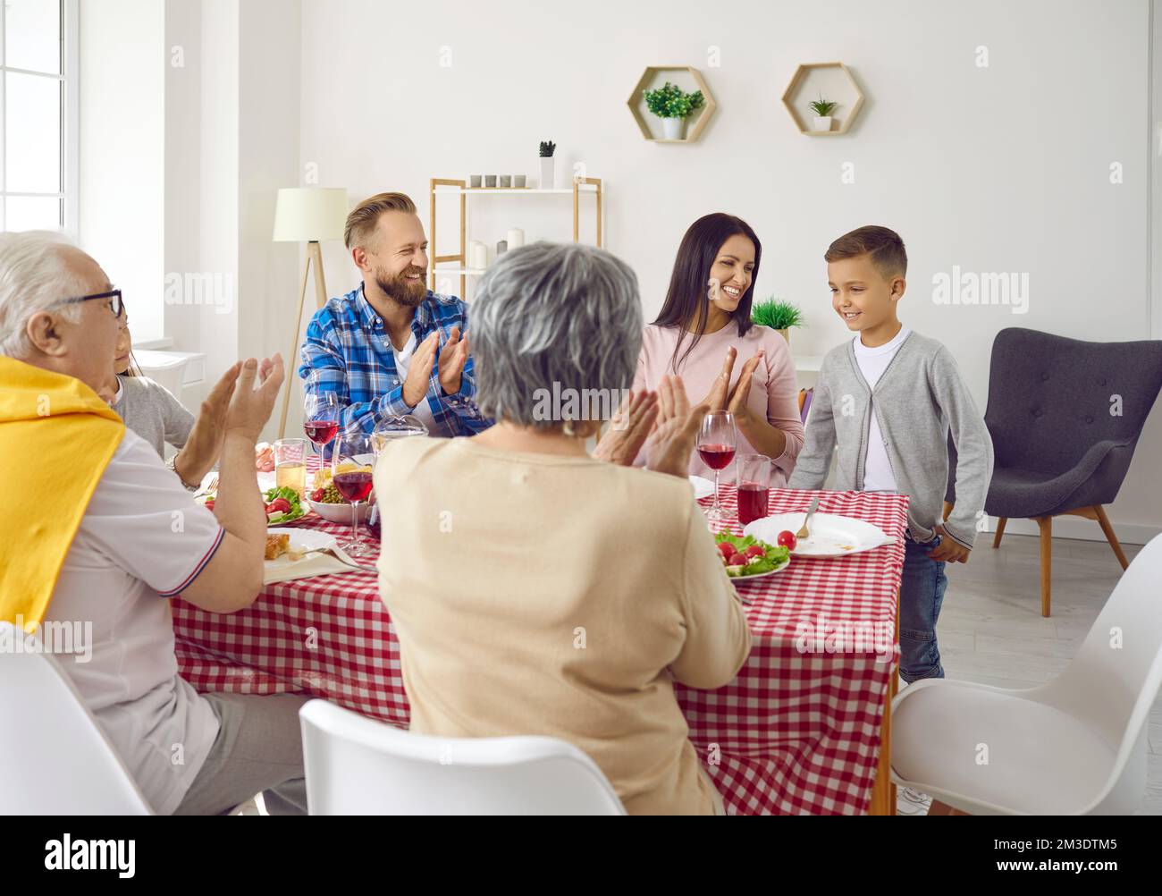 Big family congratulates child boy and clapping hands during family dinner in living room. Stock Photo