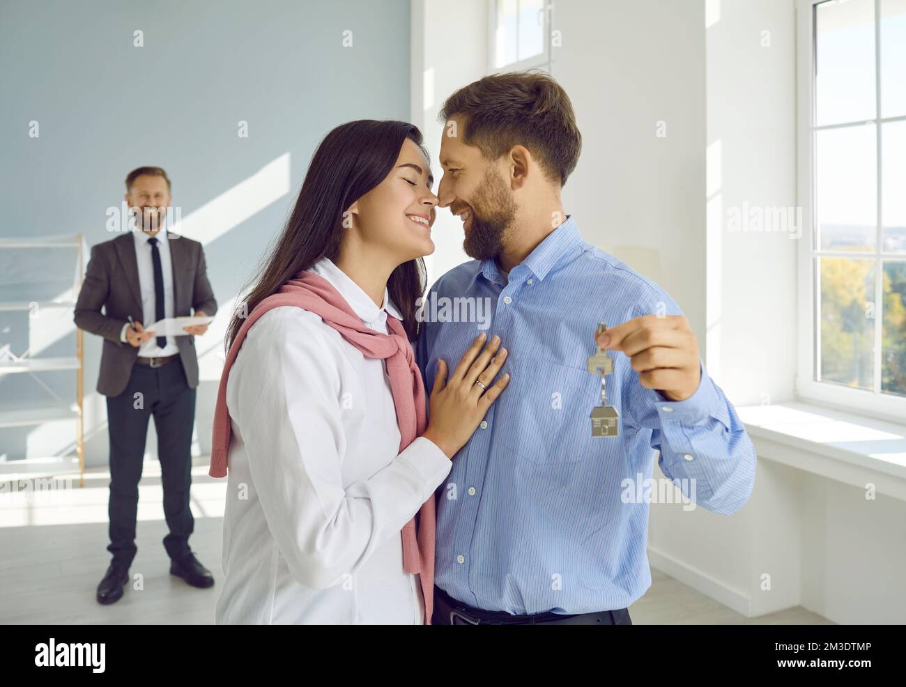 Couple in love hugs their new apartment and holds keys in their hands after buying real estate. Stock Photo