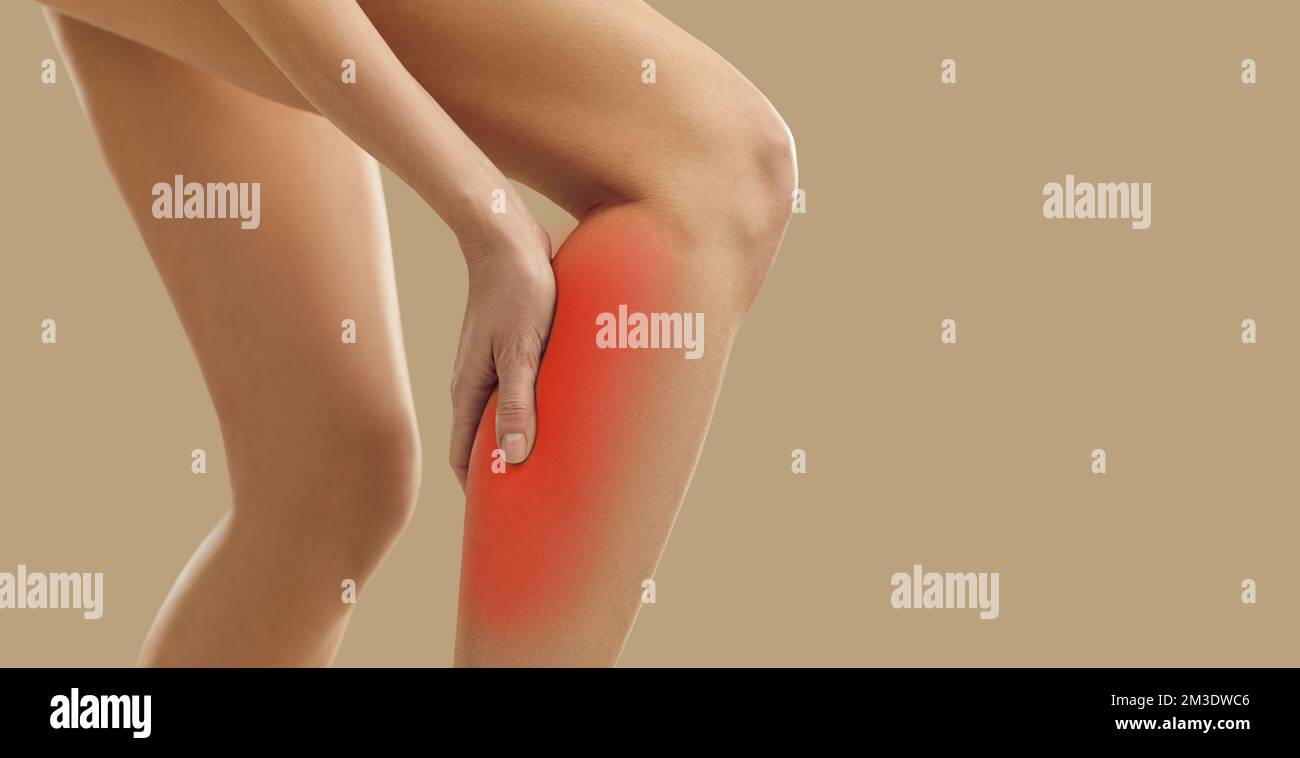 Sick or injured woman experiencing calf muscle pain standing isolated on beige background. Stock Photo