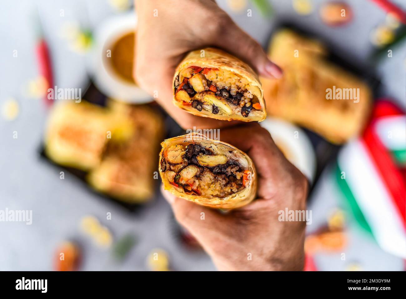 Hands holding Mexican burritos with chicken, rice, beans,cheese served