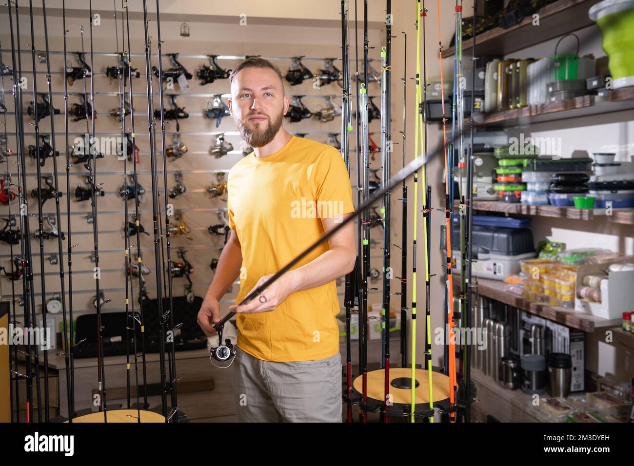 Young fisherman man chooses a fishing rod in a fishing store, copy space Stock Photo