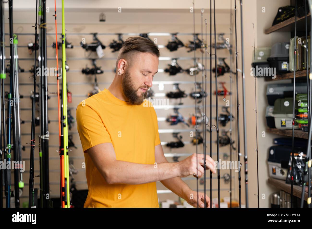Millennial man chooses fishing rod in the sports shop, copy space Stock Photo