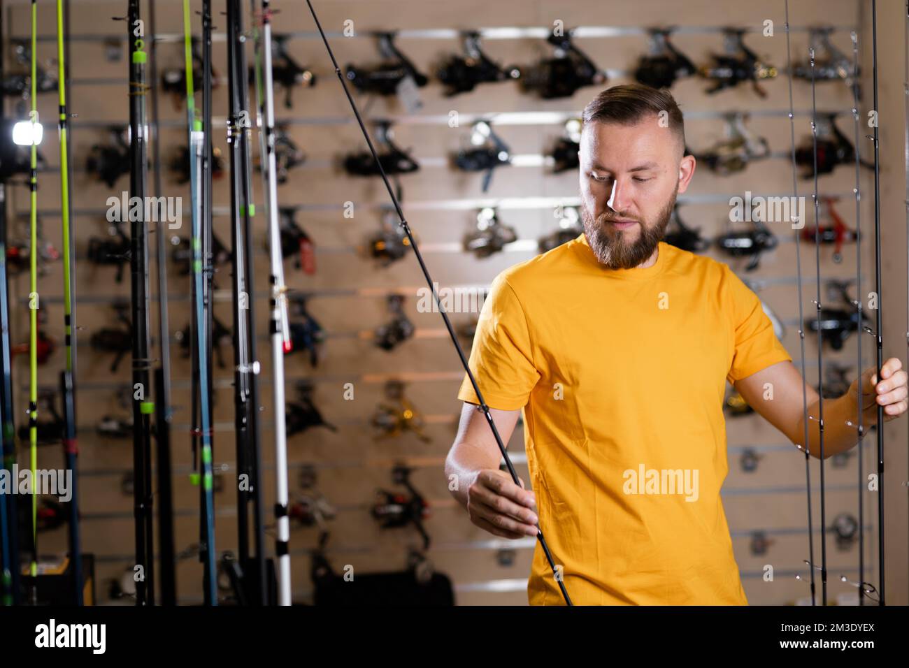 Millennial man chooses fishing rod in the sports shop, fishing store, copy space Stock Photo
