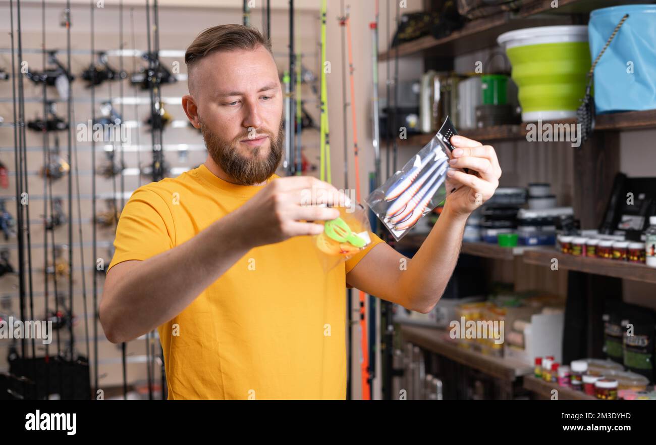 Young buyer choosing fishing accessories in the sports shop. Tackle and silicone bait for fishman. Copy space Stock Photo