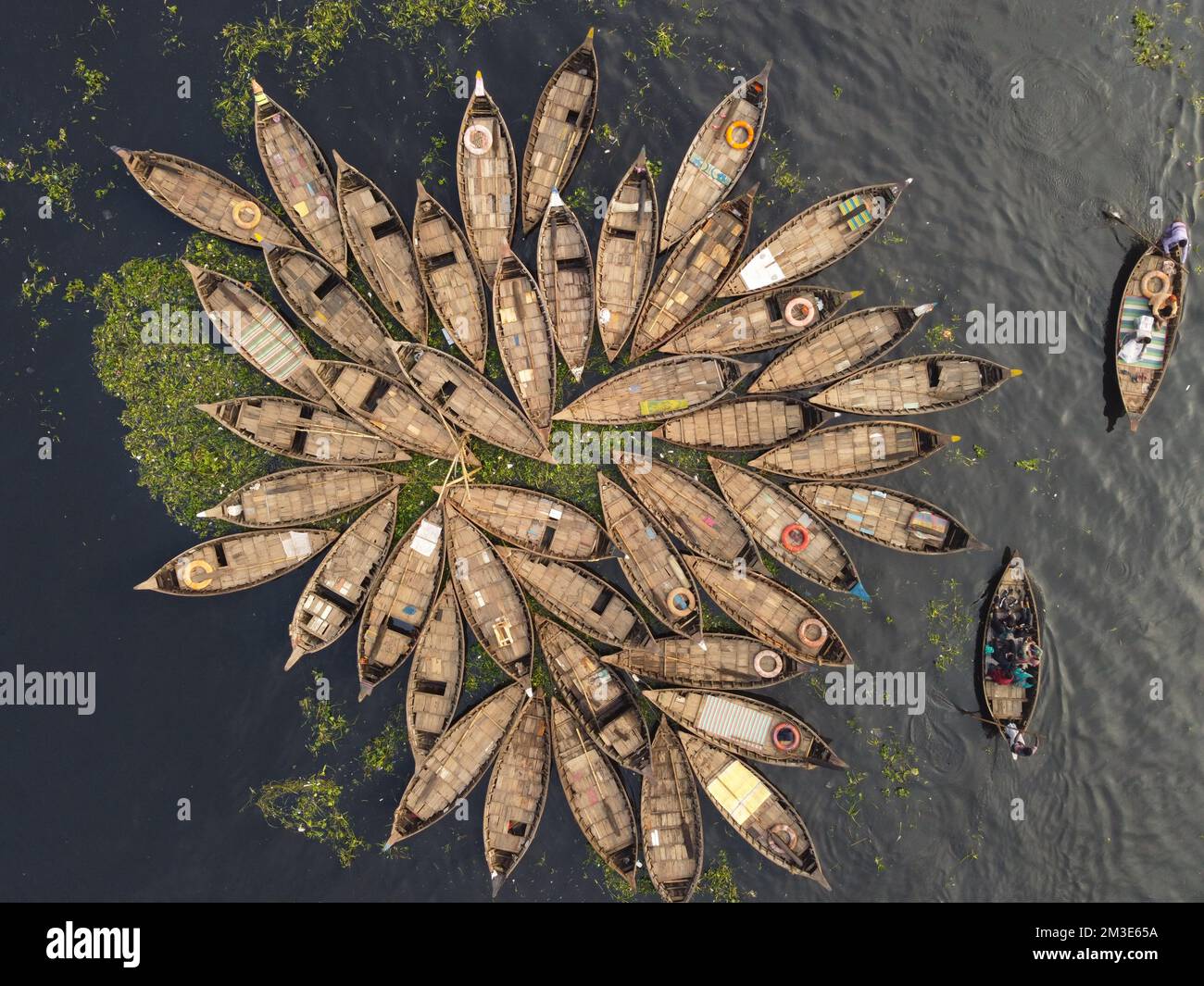 Dhaka, Bangladesh. 15th Dec, 2022. A fleet of wooden boats fans out around their moorings in the Buriganga River in Dhaka, Bangladesh. The river is widely used to transport goods, produce, and people. An estimated 50,000 commuters cross the Buriganga from Keraniganj to work in Dhaka, and many take boats. Hundreds of small boats, called 'Dinghy Noukas', are moored in the river port of Dhaka, the capital of Bangladesh. In them, ferrymen transport workers, goods, and tourists across the Buriganga River every day. Credit: Joy Saha/Alamy Live News Stock Photo