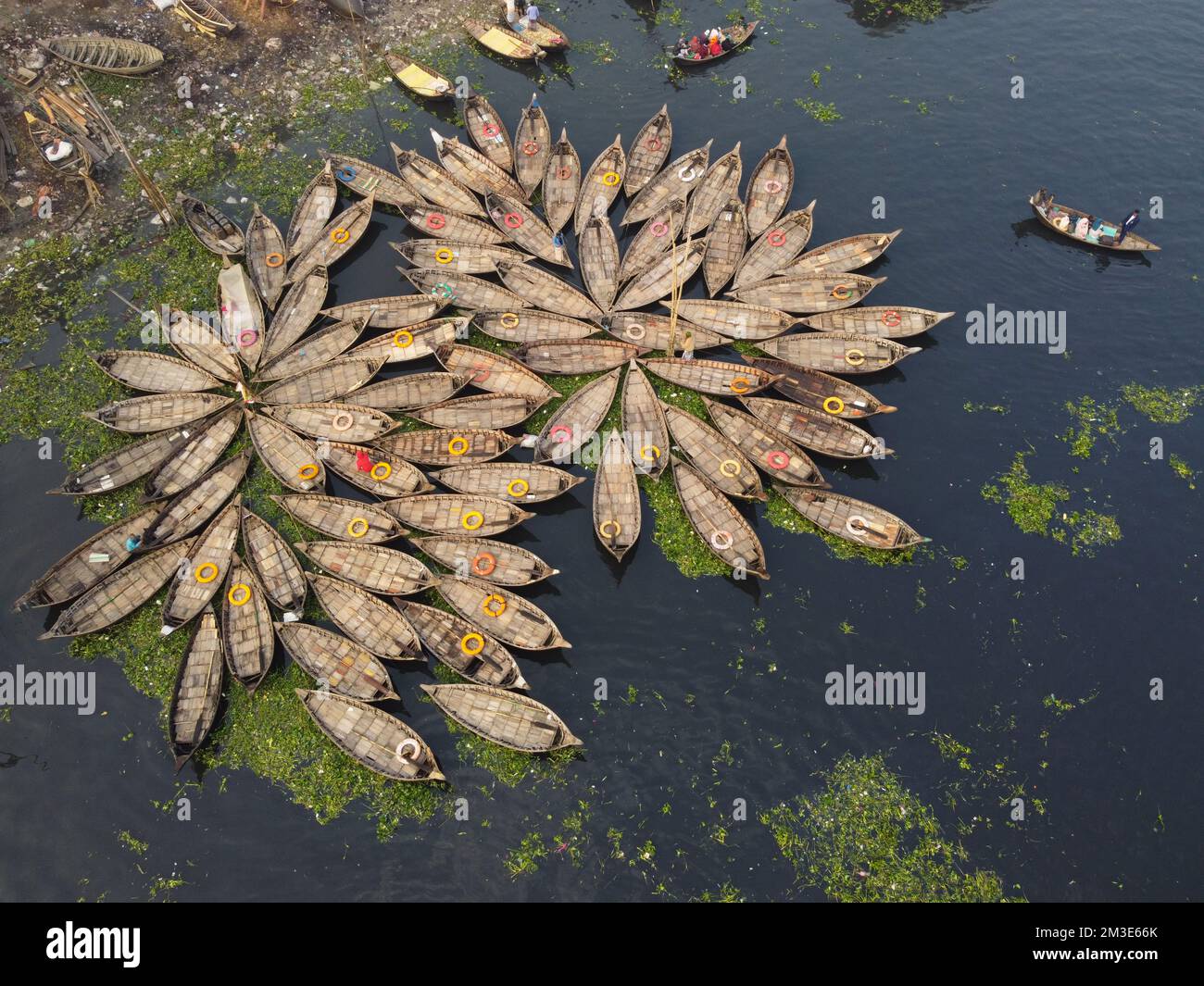 Dhaka, Bangladesh. 15th Dec, 2022. A fleet of wooden boats fans out around their moorings in the Buriganga River in Dhaka, Bangladesh. The river is widely used to transport goods, produce, and people. An estimated 50,000 commuters cross the Buriganga from Keraniganj to work in Dhaka, and many take boats. Hundreds of small boats, called 'Dinghy Noukas', are moored in the river port of Dhaka, the capital of Bangladesh. In them, ferrymen transport workers, goods, and tourists across the Buriganga River every day. Credit: Joy Saha/Alamy Live News Stock Photo