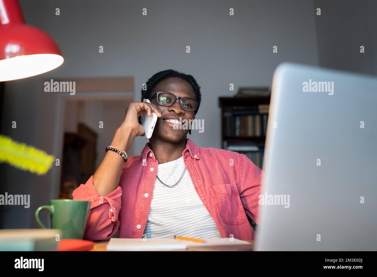 Friendly young African man freelance consultant talking to client on phone while working from home Stock Photo
