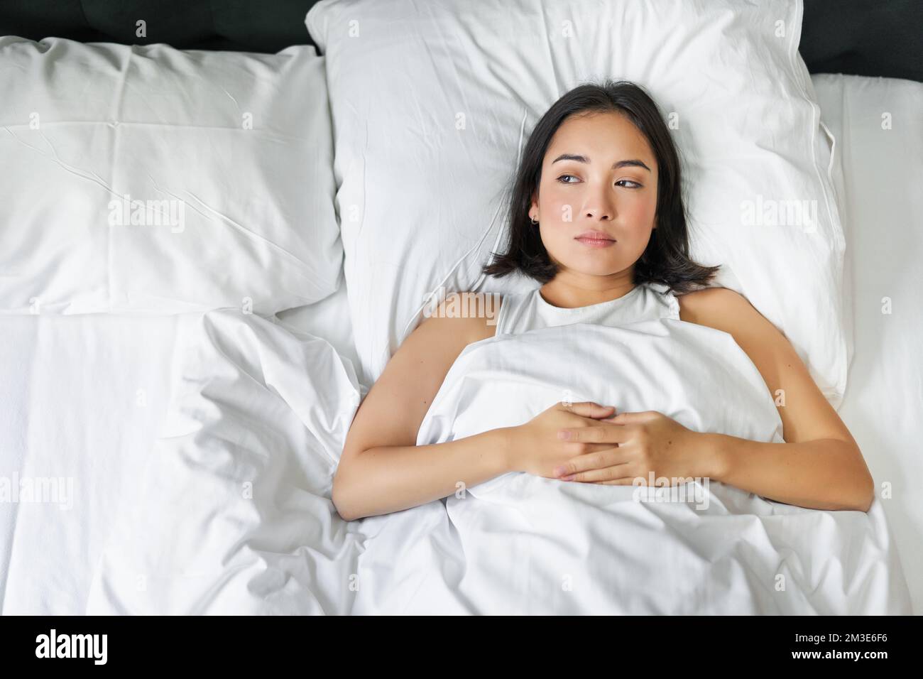 Portrait of asian girl lying alone in bed with white sheets bedding