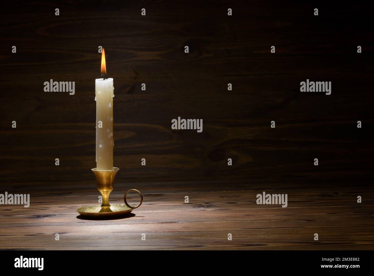 burning old candle with vintage brass candlestick on wooden background