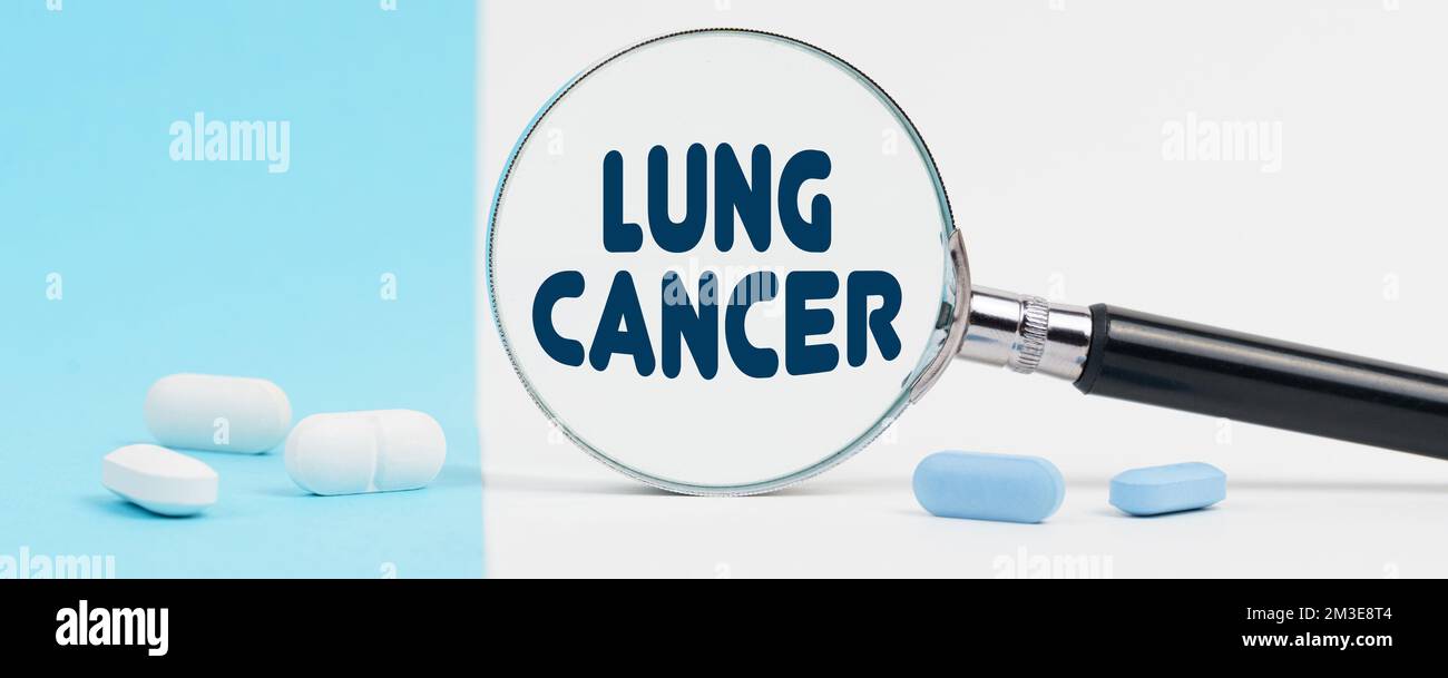 Medicine and health concept. On a blue and white background, there are pills and a magnifying glass, inside of which it is written - LUNG CANCER Stock Photo