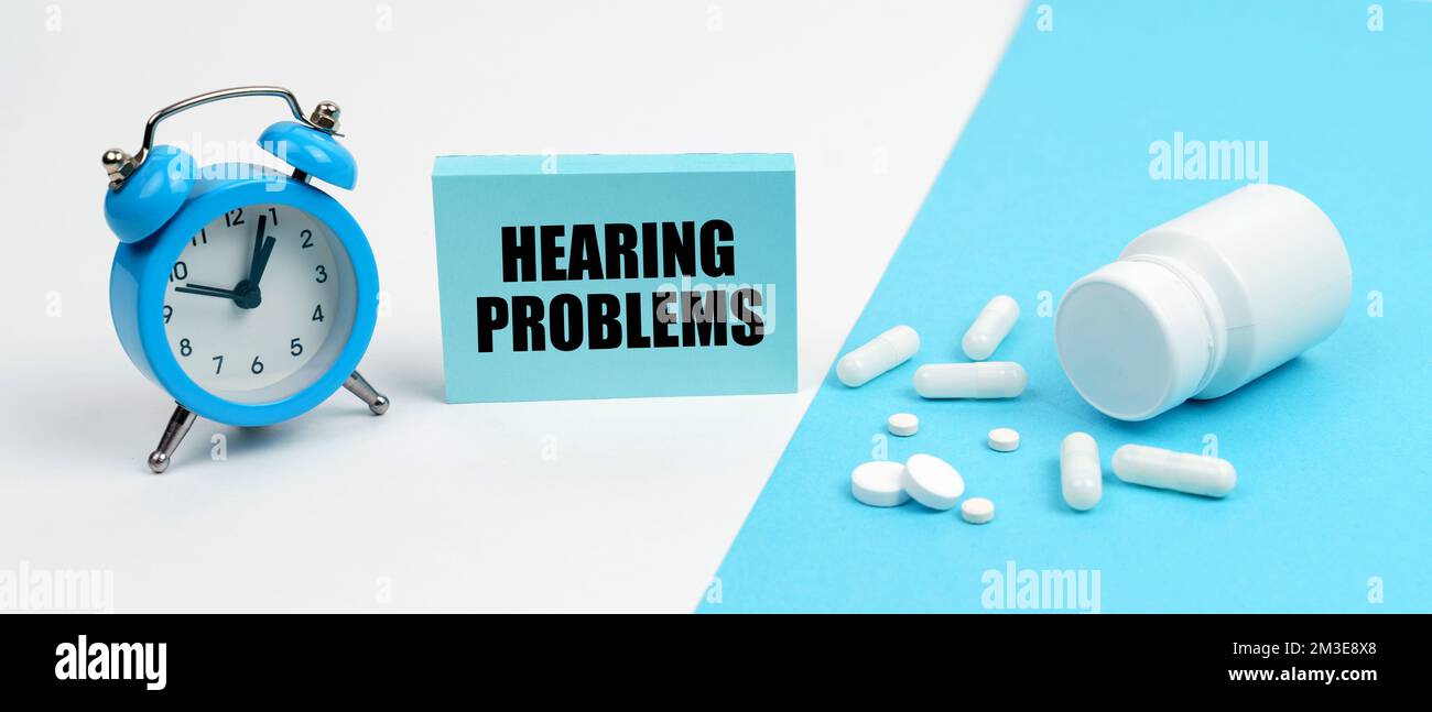 Medicine and health concept. On a blue surface are pills, on a white surface an alarm clock and a plate with the inscription - Hearing Problems Stock Photo