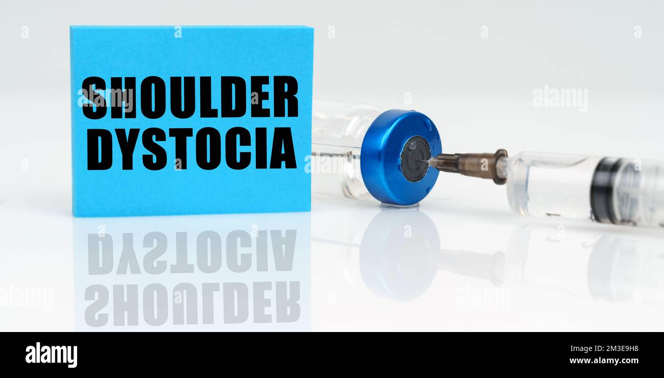 Medicine concept. On a white reflective surface are a syringe, an injection and a blue plaque that says - Shoulder Dystocia Stock Photo