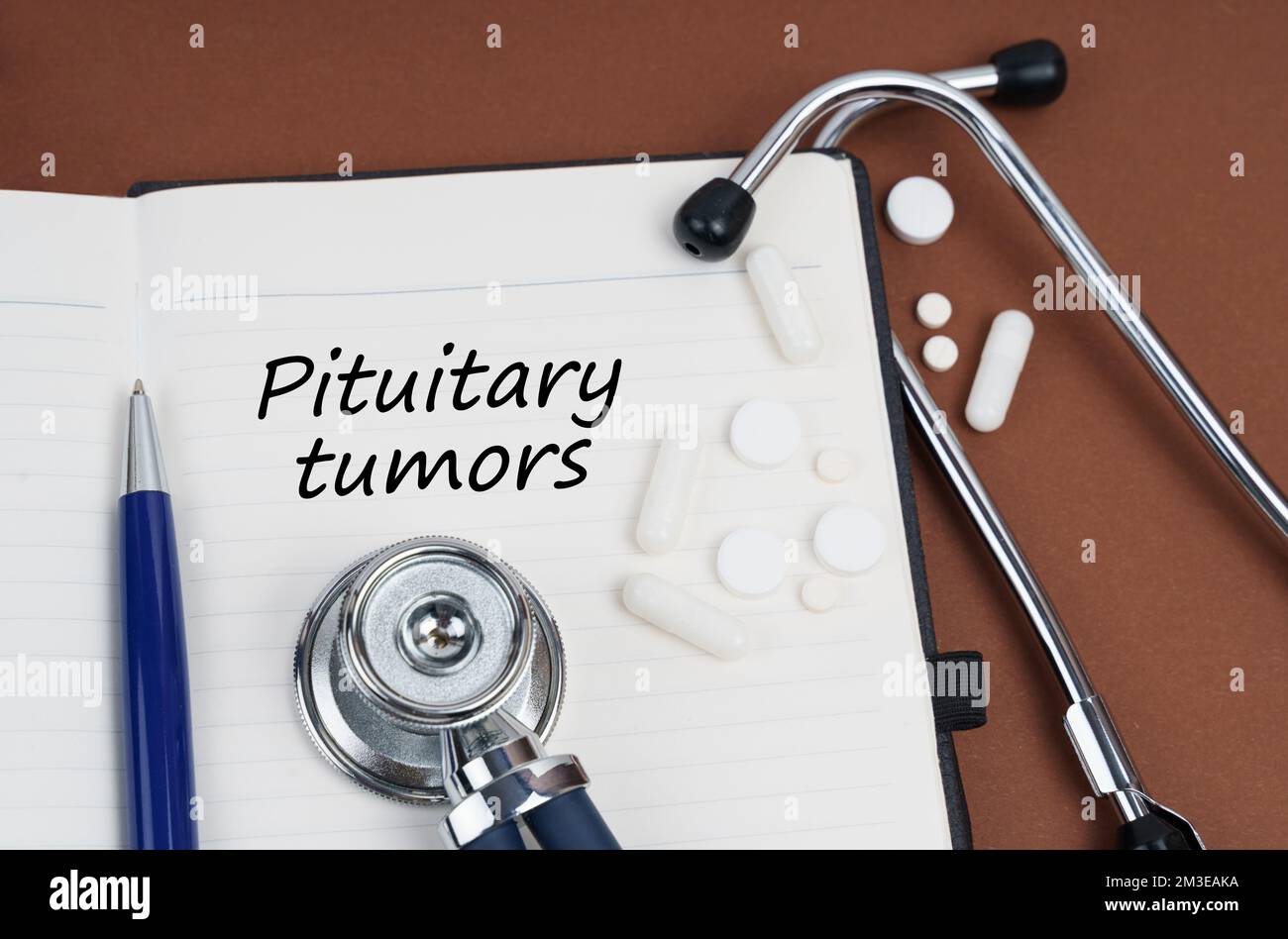 Medicine and health concept. On a brown surface lie pills, a pen, a stethoscope and a notebook with the inscription - pituitary tumors Stock Photo