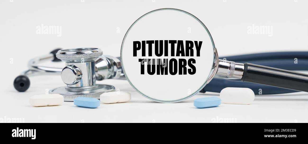 Medicine and health concept. On a white surface are pills, a stethoscope and a magnifying glass inside which is written - pituitary tumors Stock Photo
