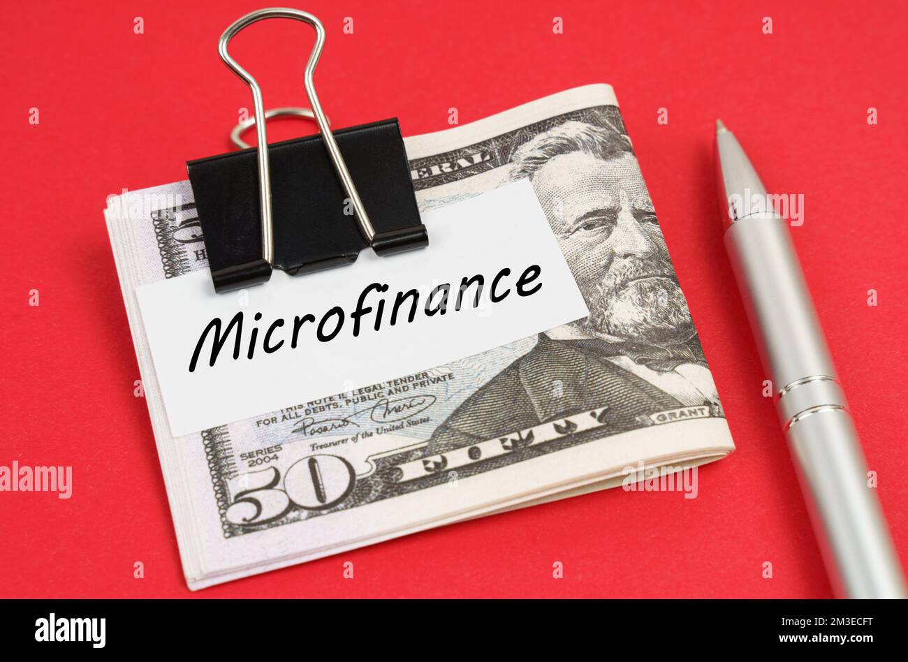 Finance and business concept. On a red background lies a pen and dollars clamped with a clip with the inscription on paper - Microfinance Stock Photo