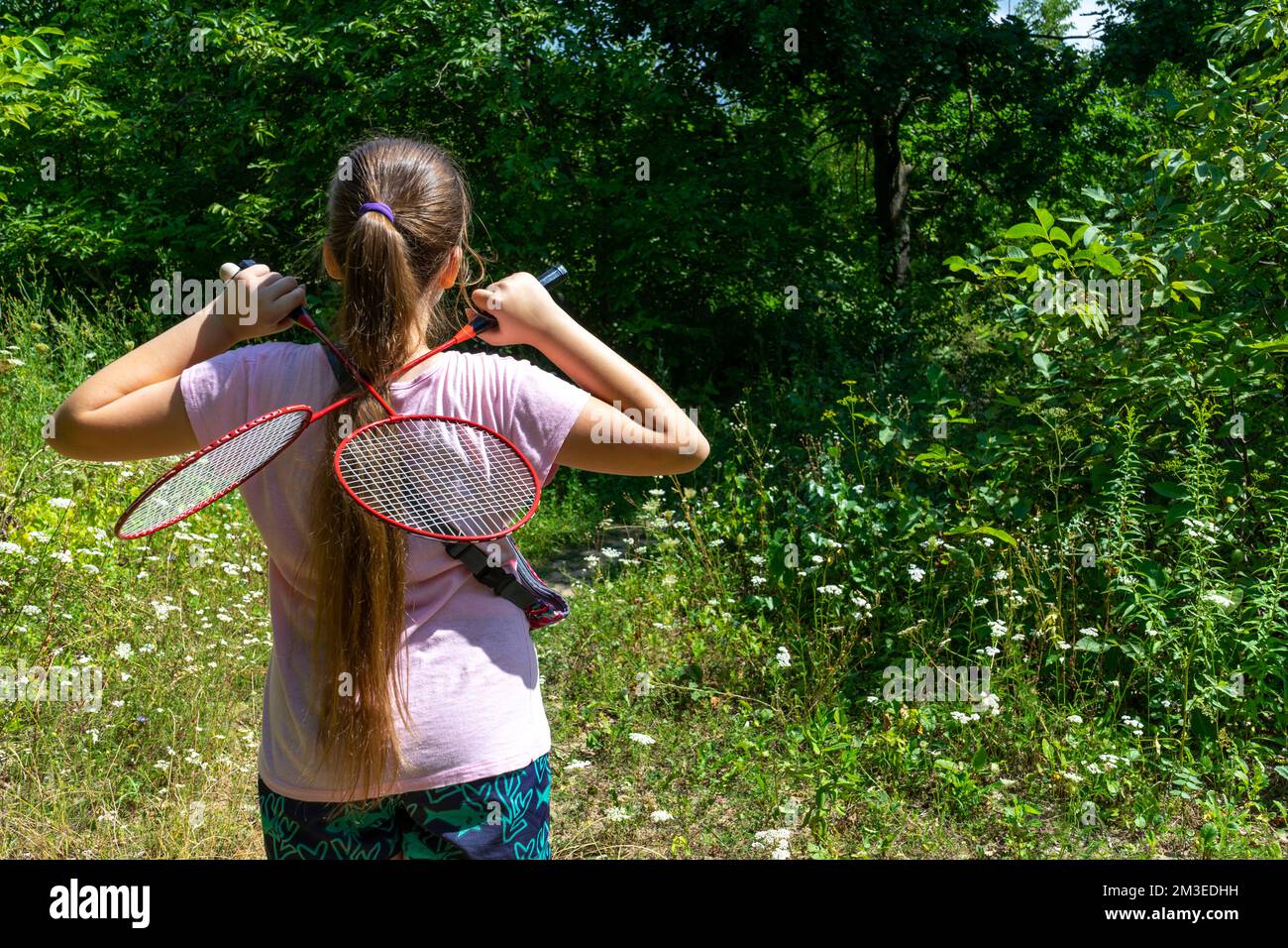 A girl stands in a forest clearing with two tennis rackets crossed on her back Stock Photo