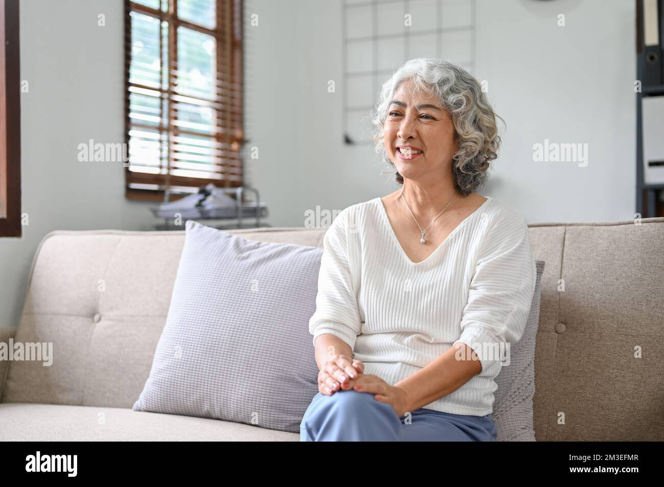 Happy 60yearold elderly retire woman sits on sofa in her living room
