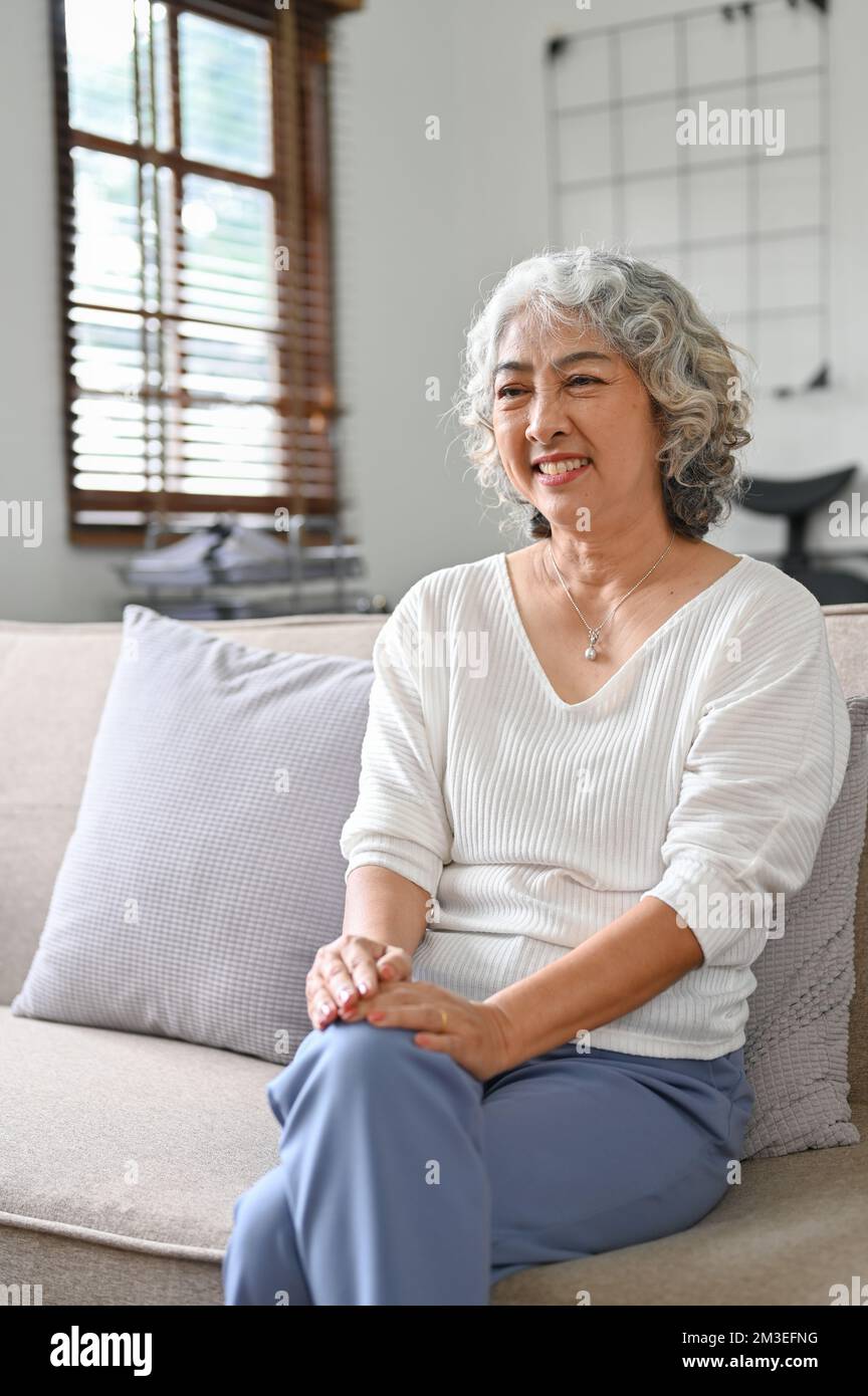 Portrait, Happy 60yearold elderly retire woman sits on sofa in her living room, enjoy watching