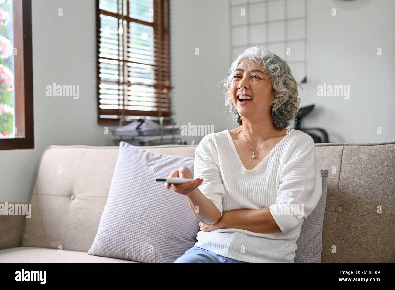 Cheerful and happy 60yearold elderly retire woman sits on sofa in her