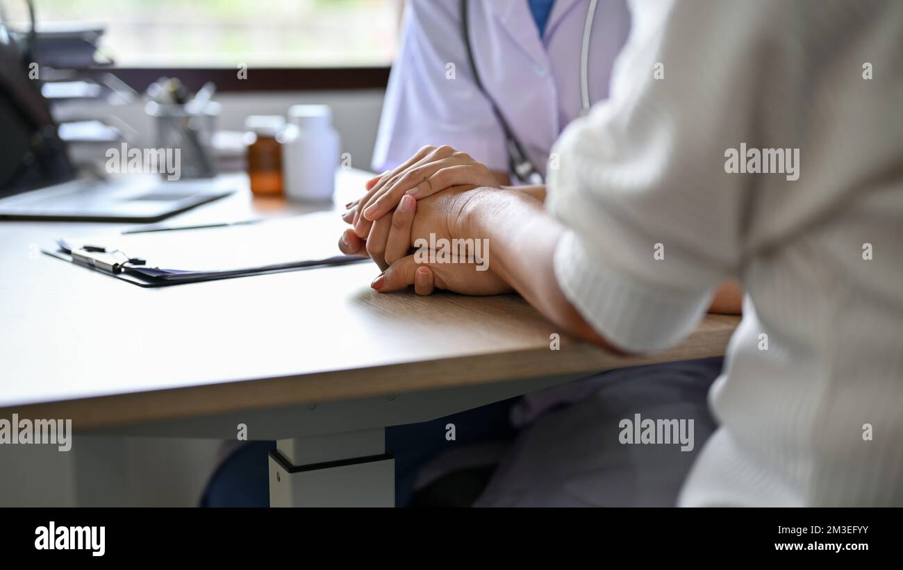 close-up image, A female doctor holding her patient's hands on the table while discussing the treatment plan. Stock Photo