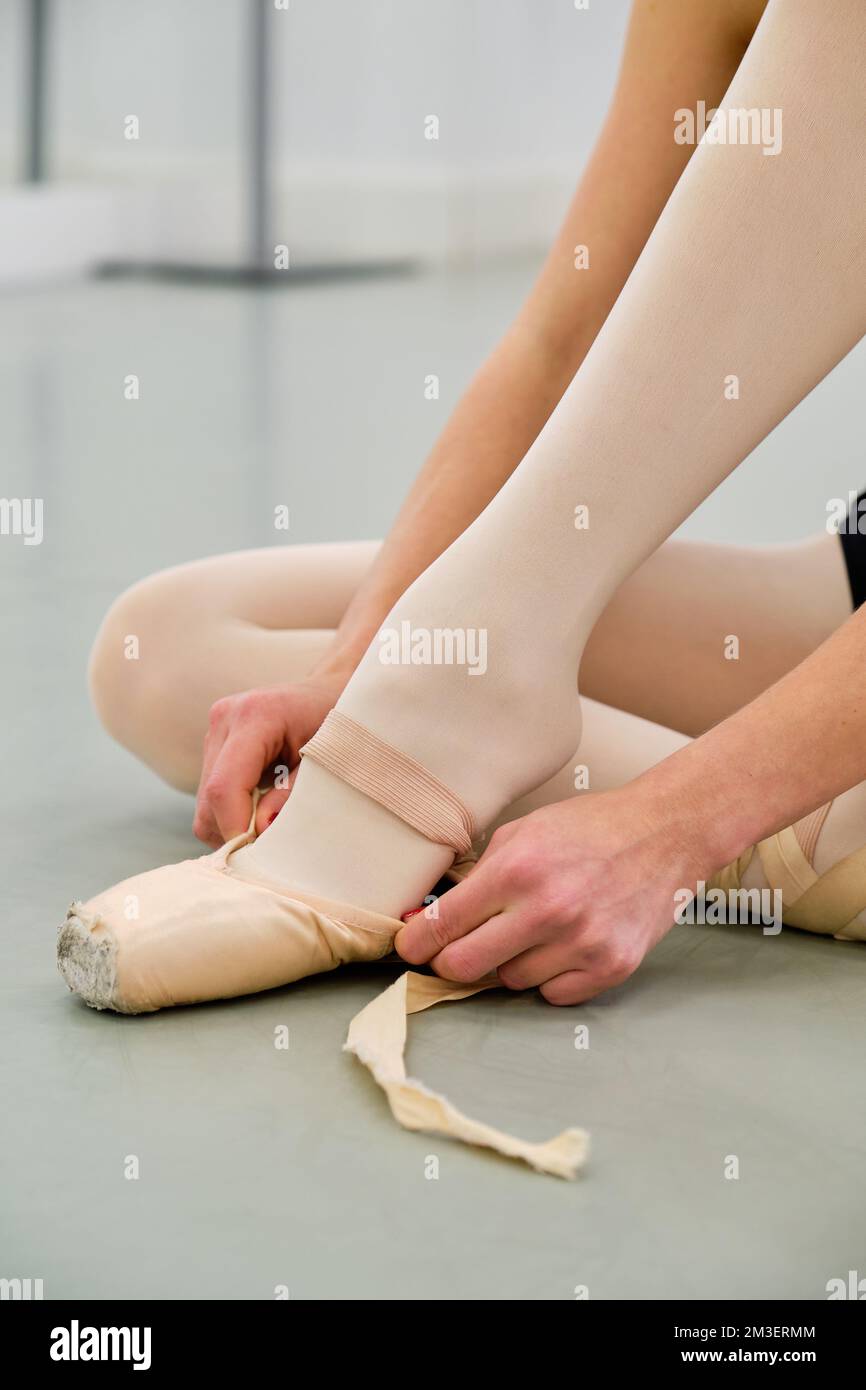 Ballerina putting on the ballet pointe shoes sitting on the floor. Stock Photo