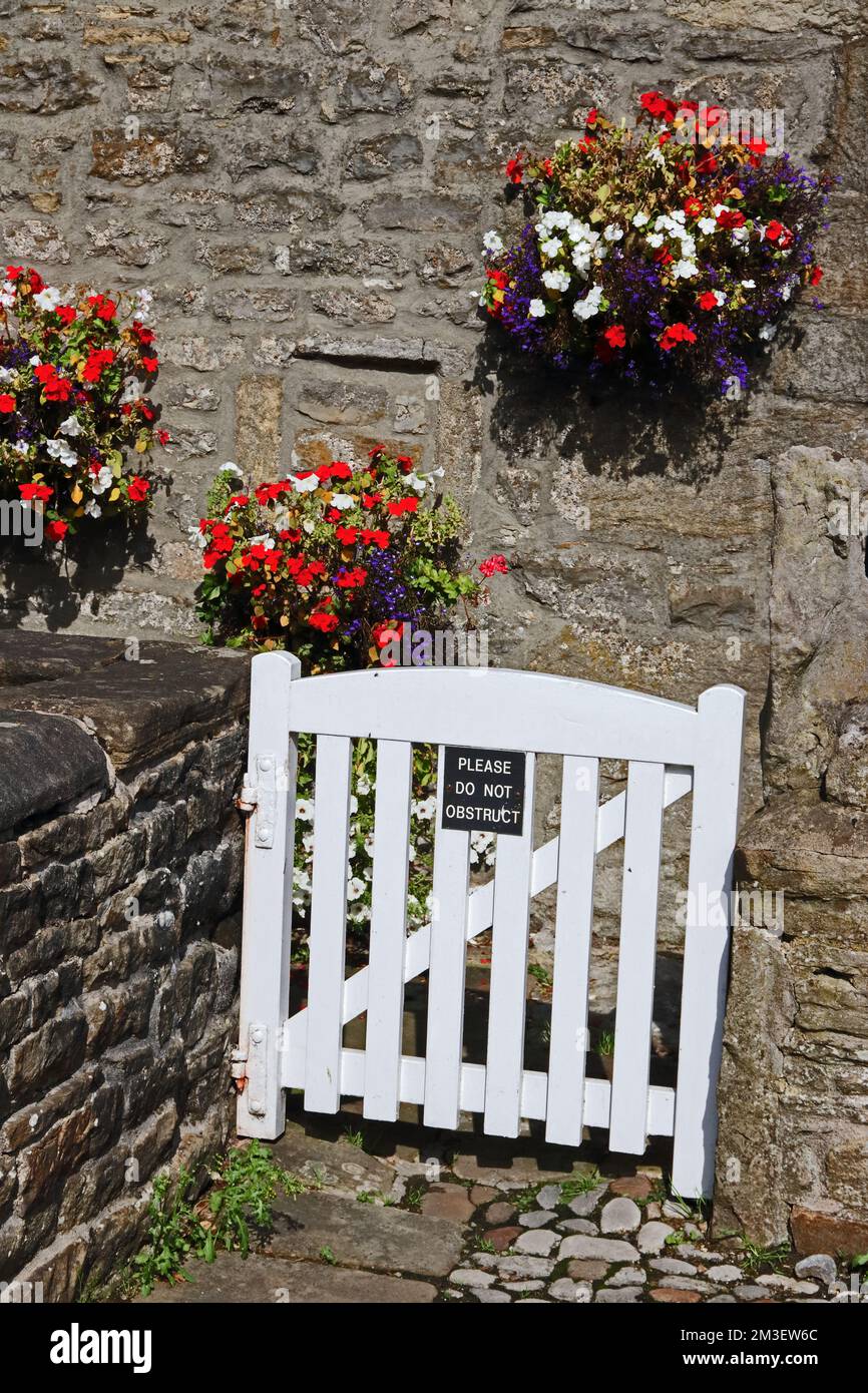 Do not obstruct sign on white wooden gate with colourful hanging baskets behind, Stock Photo