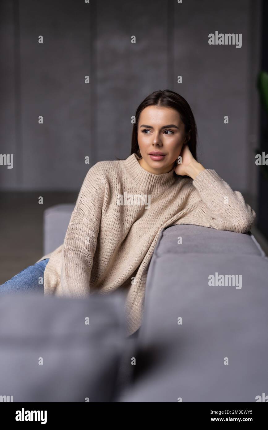 Happy young woman sitting on sofa at home and looking at camera ...