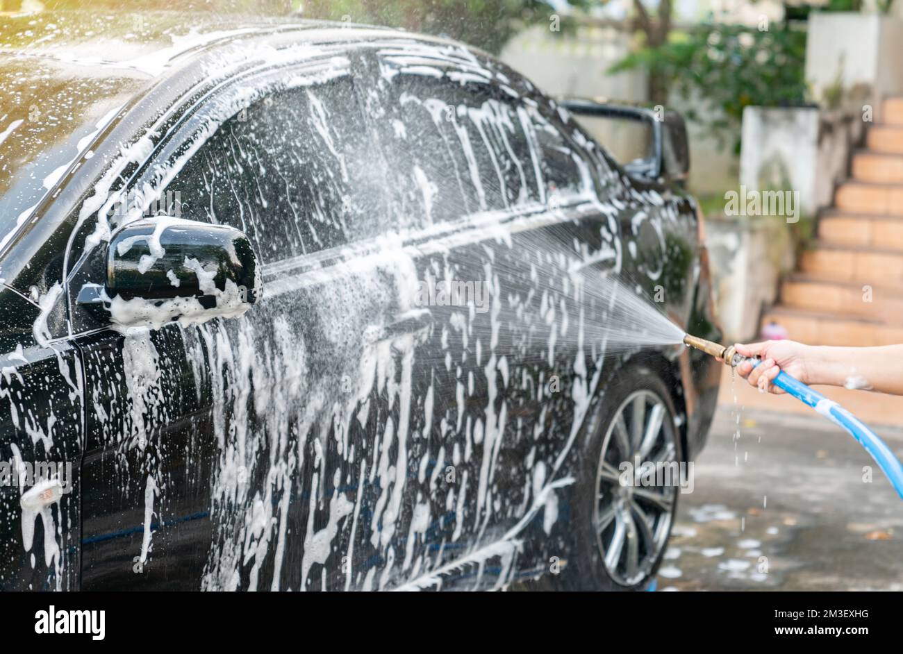 A woman washes her black sports car in a manual car wash at home. Car
