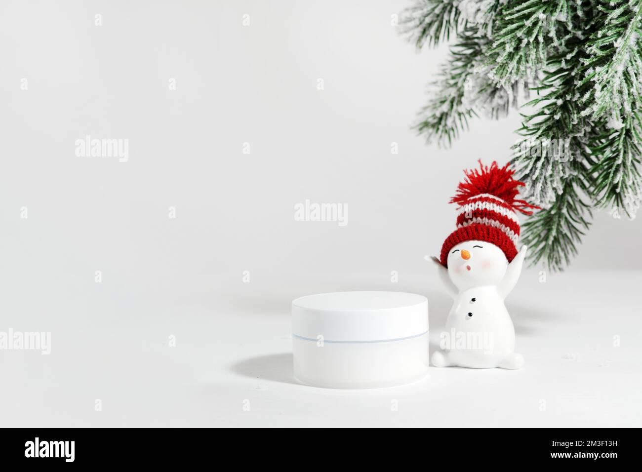 White jar of skin care cosmetics on a white surface with a snowman. Winter cosmetics. Empty container with fir branches background. Christmas gift ide Stock Photo