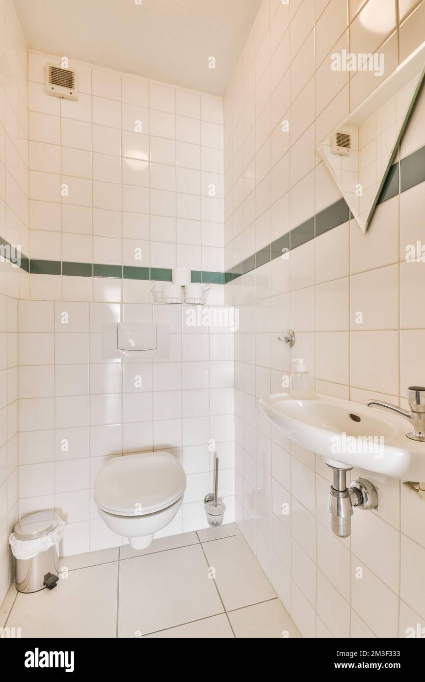 https://c8.alamy.com/comp/2M3F333/a-small-bathroom-with-white-tiles-and-green-trim-on-the-walls-along-with-a-toilet-in-the-corner-next-to-the-sink-2M3F333.jpg