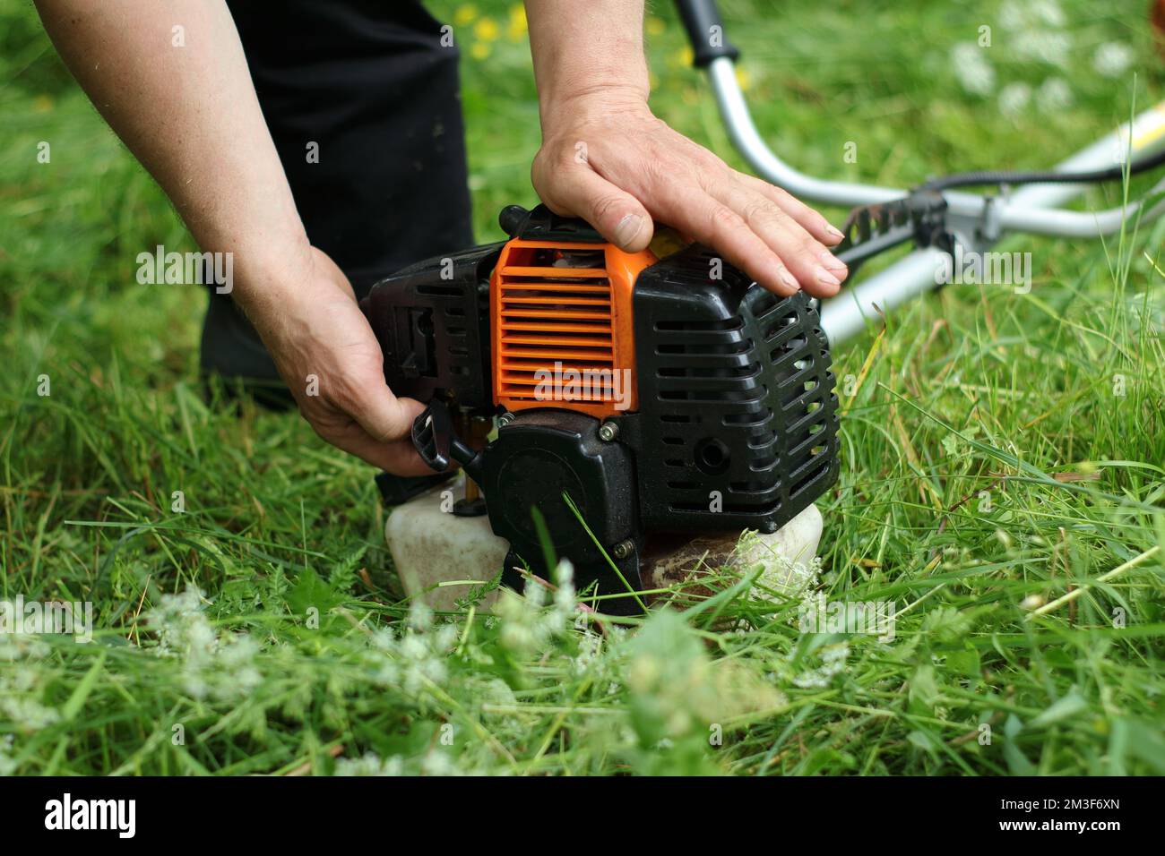a person fires a petrol brush cutter against the background of a lawn Stock Photo