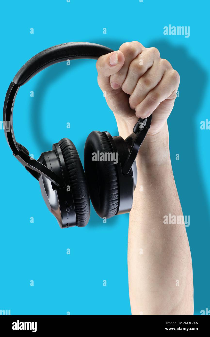 black wireless headphones in hand on a blue background Stock Photo