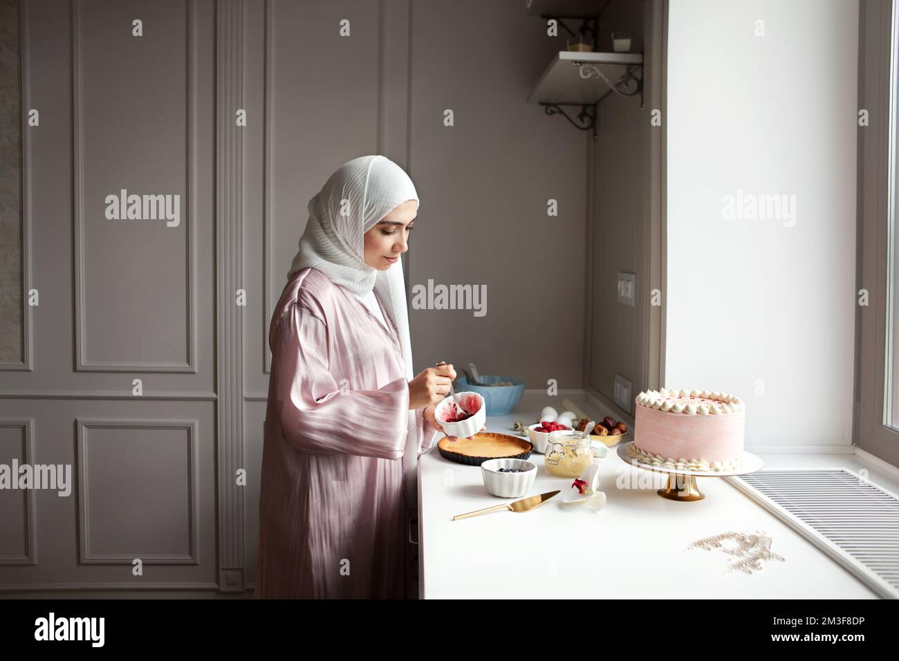 Muslim woman cooks dessert cake at home kitchen, arabian young model in hijab and abaya Stock Photo