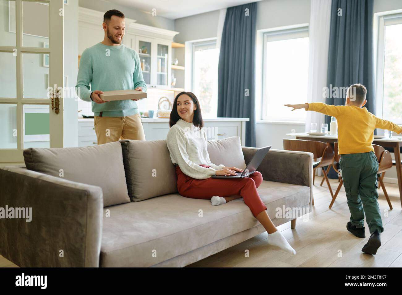 Wife working on laptop while husband orders pizza for lunch Stock Photo