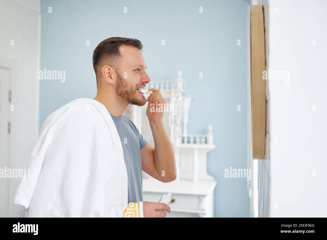 Man brushing teeth in bathroom looking at mirror side view shot Stock Photo